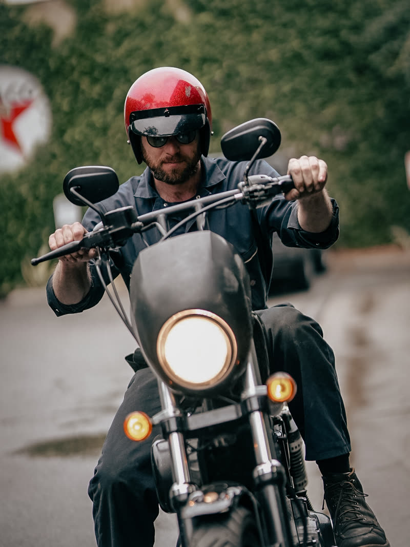 Rider on a cafe racer in the wet, red helmet, road still shining