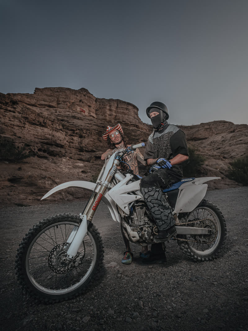 Two figures and the bike against the canyon wall at dusk