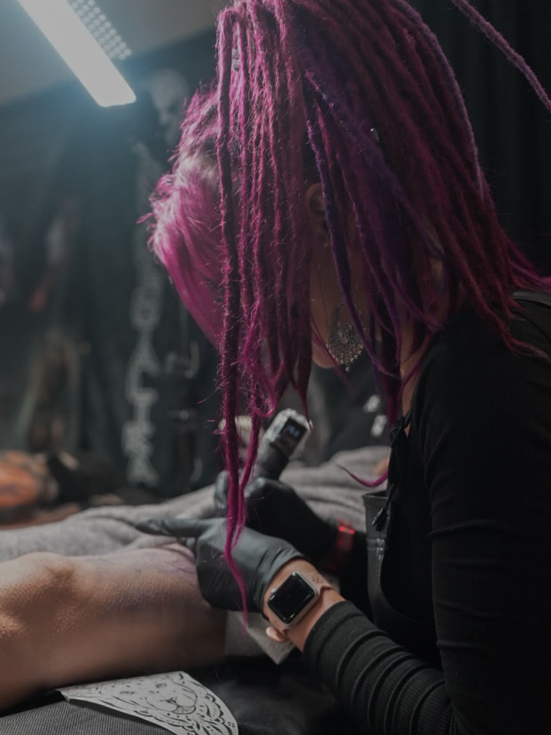 Nairadots tattooing, pink dreadlocks falling over the work