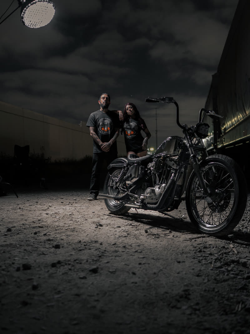 Two figures and the bike lit by a single flash under a storm sky