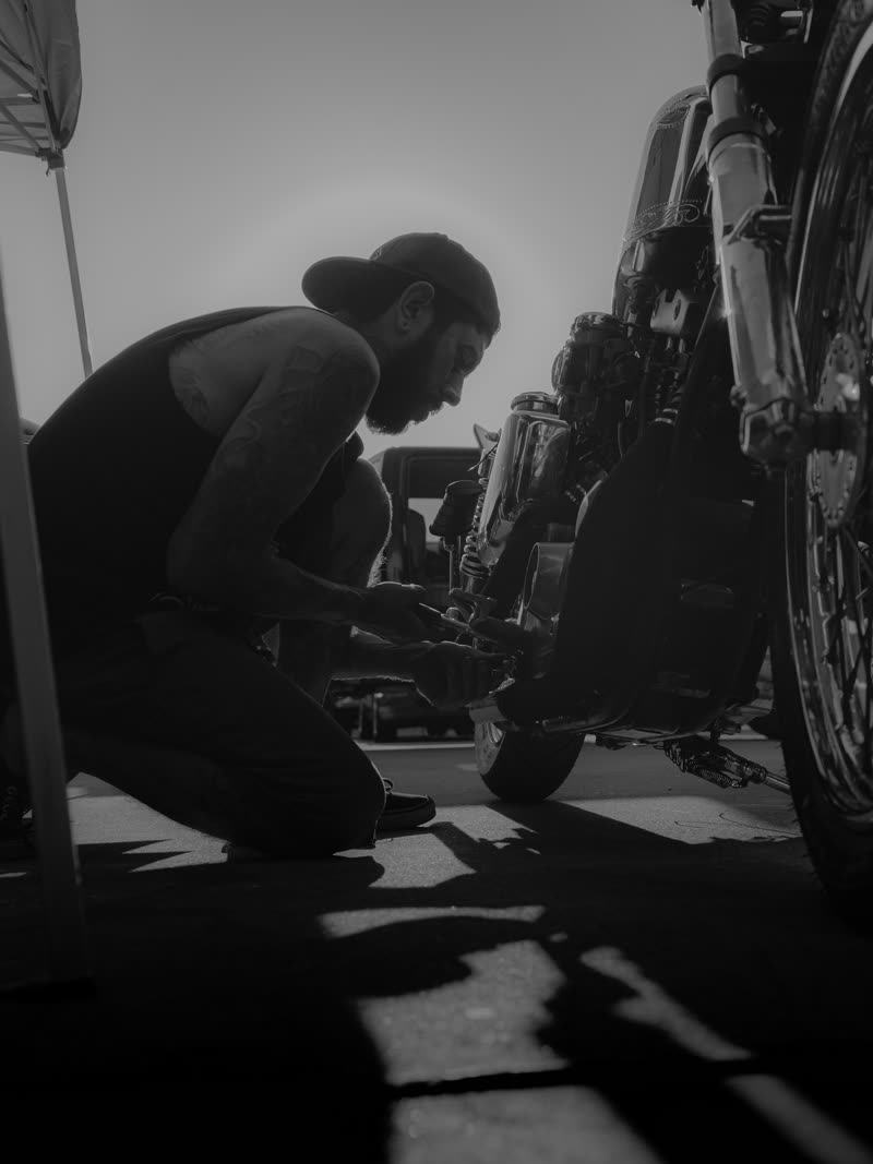 Kneeling to work under the bike in hard sun, long shadow across the lot
