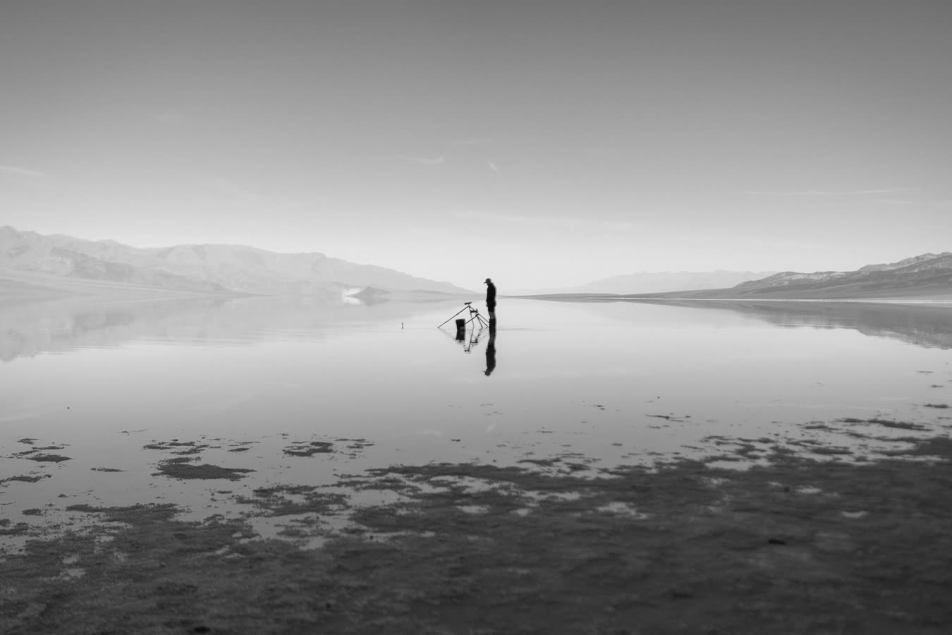 A lone figure and a tripod on the flooded pan, the range mirrored around them