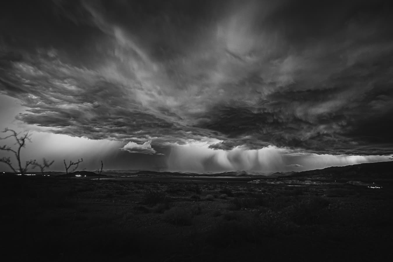 A storm cell dragging rain curtains across the desert, black and white