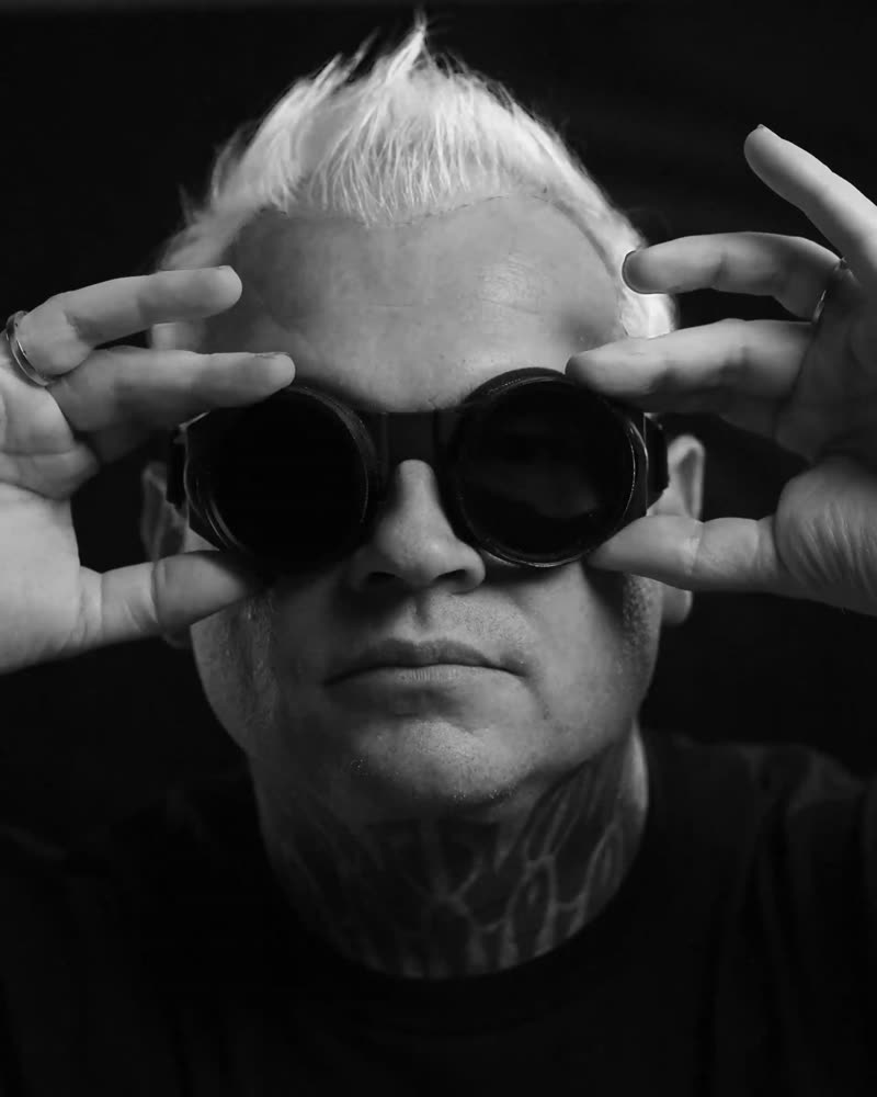 Black and white portrait, hands raised to blacked-out goggles